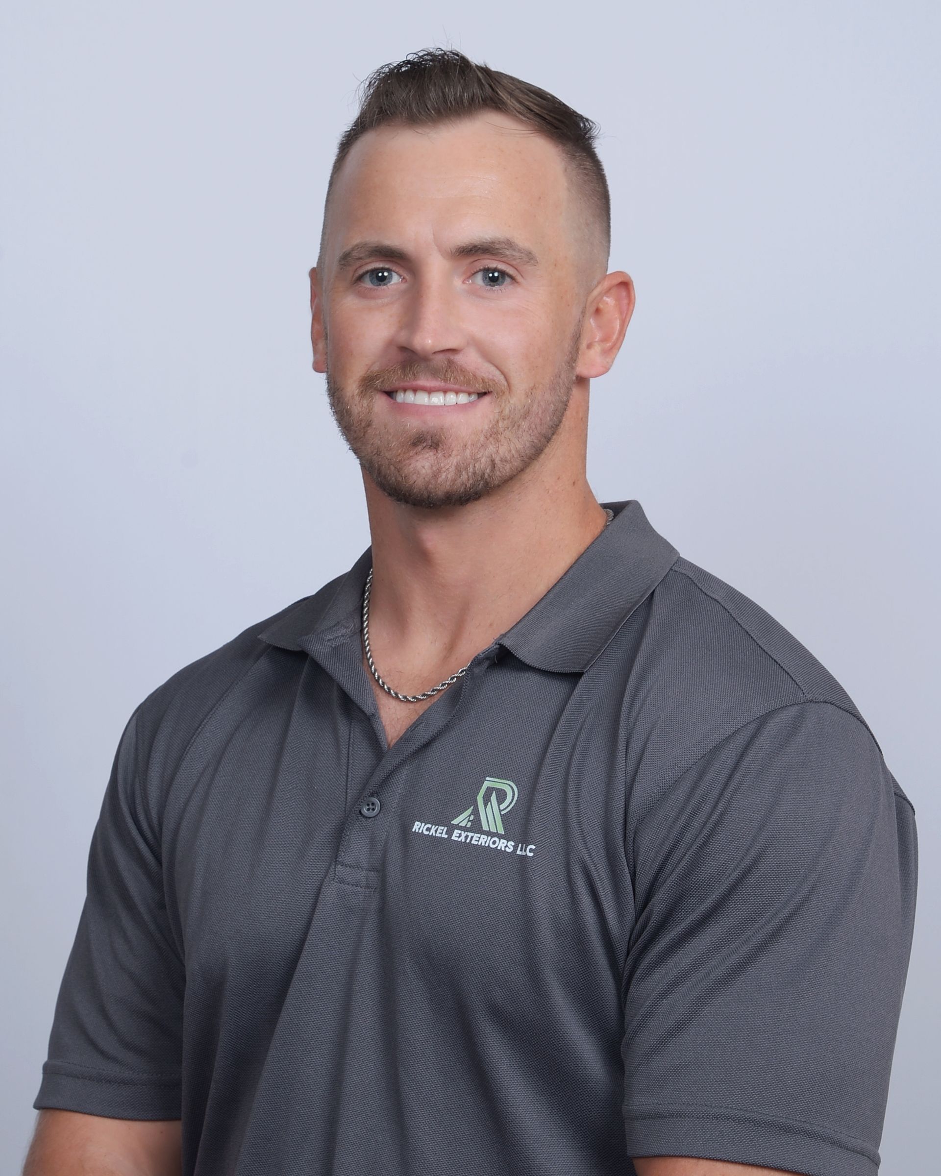 Man in gray polo shirt, smiling, with short brown hair, facing forward.