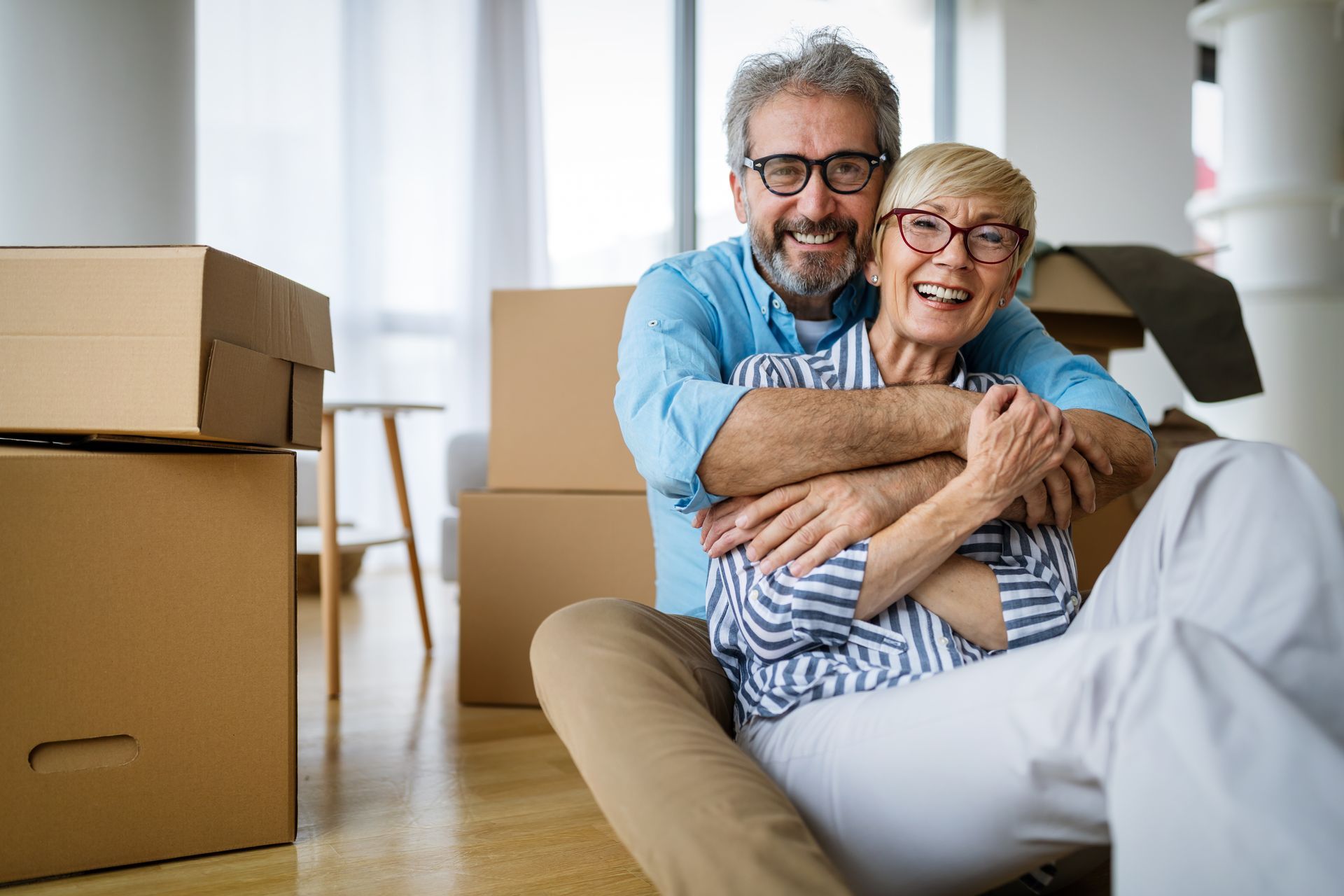 Couple embracing, smiling, surrounded by moving boxes, inside a home.