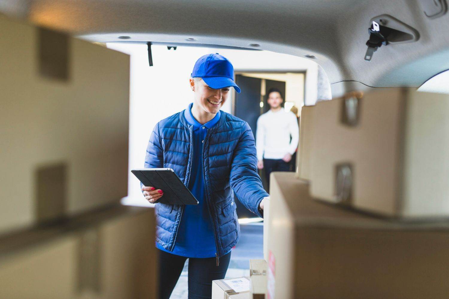 A delivery man is loading boxes into the back of a car.