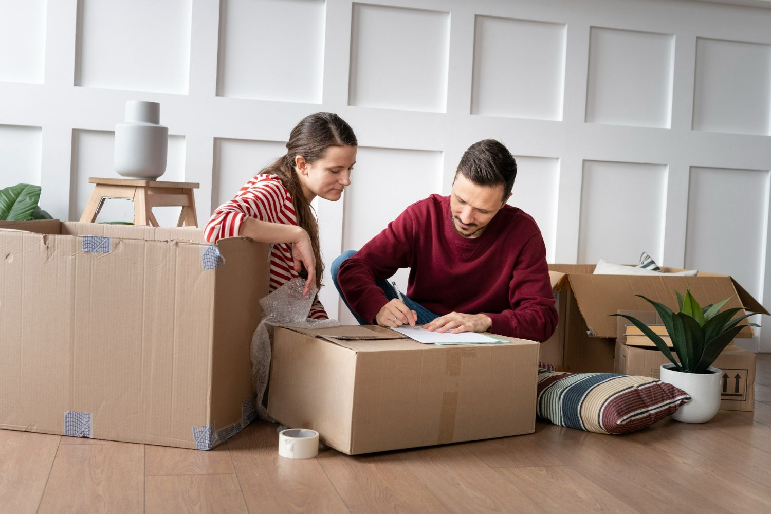 A man and a woman are sitting on cardboard boxes in a living room.