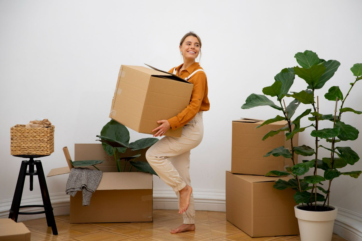 A woman is carrying a cardboard box in a room filled with cardboard boxes.