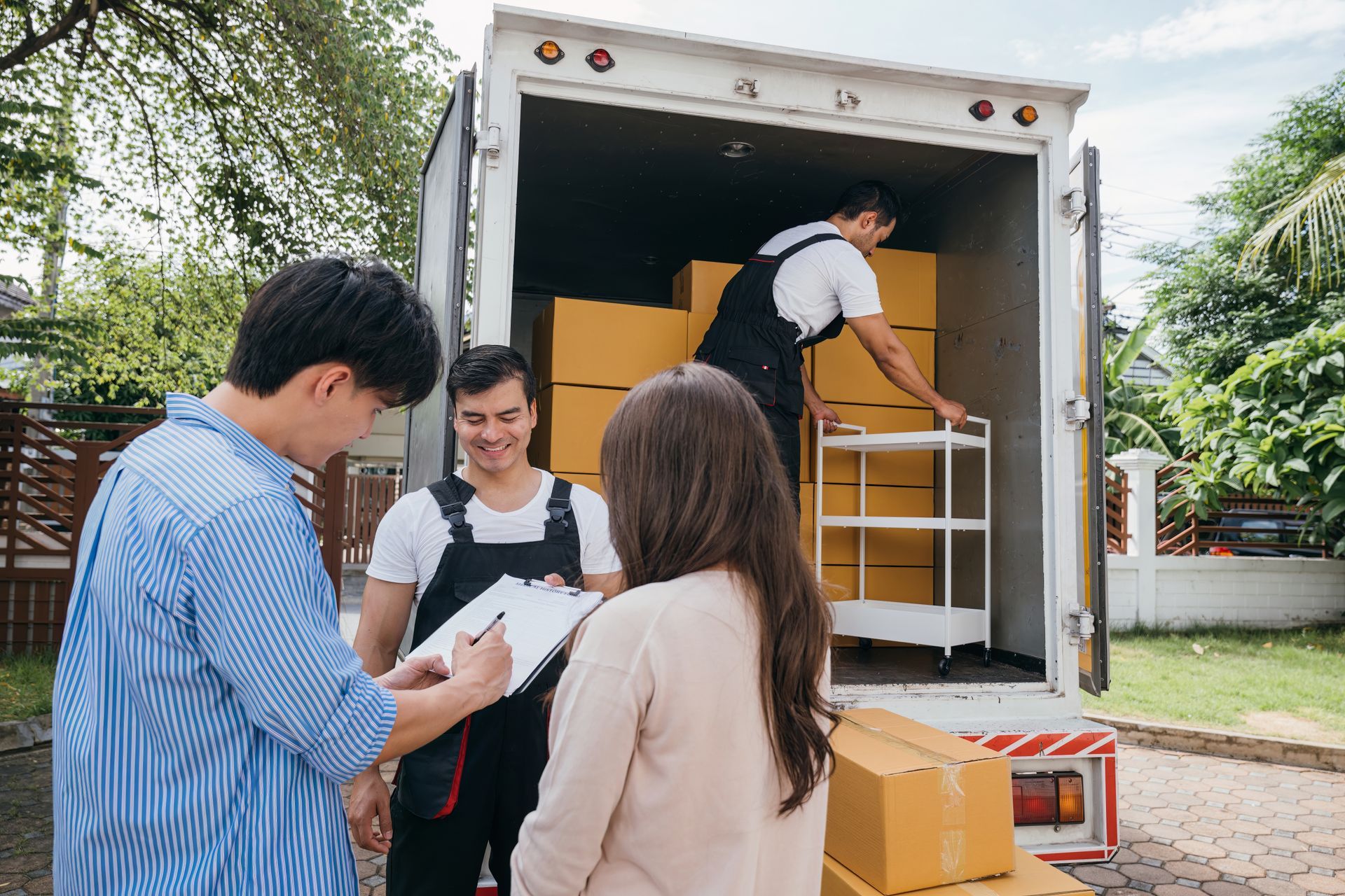 People signing a form with movers near a moving truck filled with boxes.