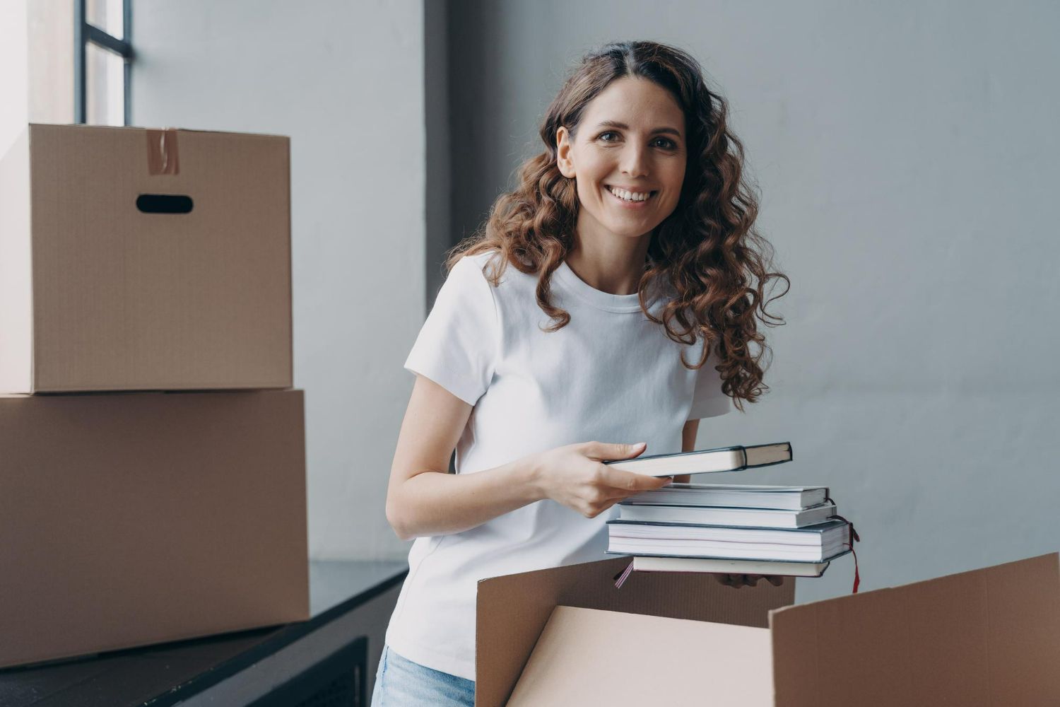 A woman is holding a stack of books in a cardboard box.