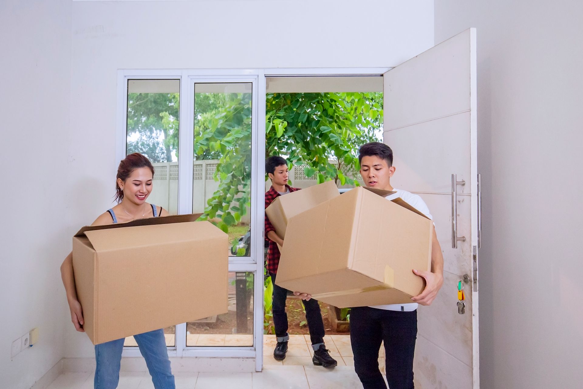 A man and a woman are carrying cardboard boxes into a house.