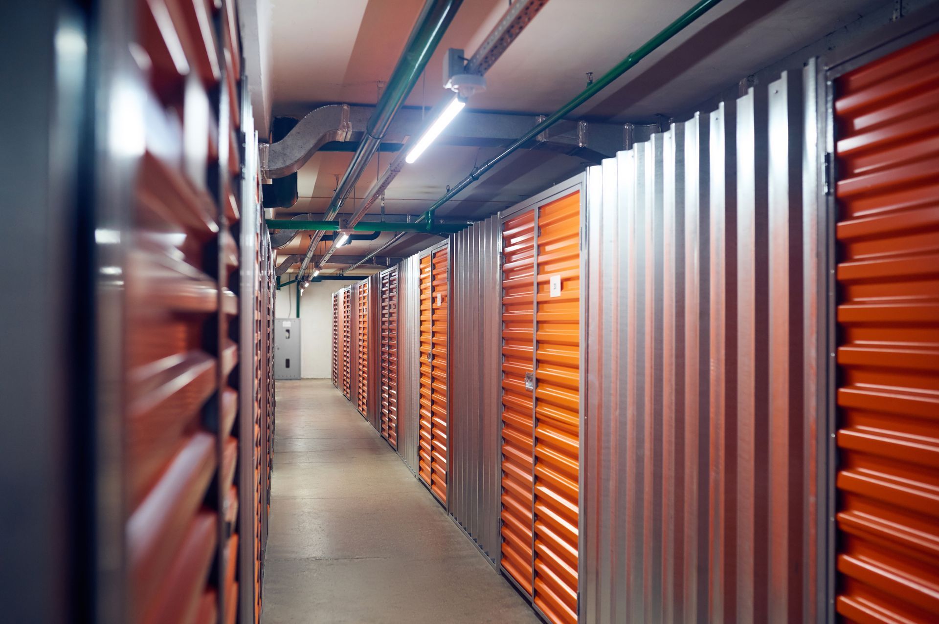 A long hallway with orange shutters on the doors of a storage unit.