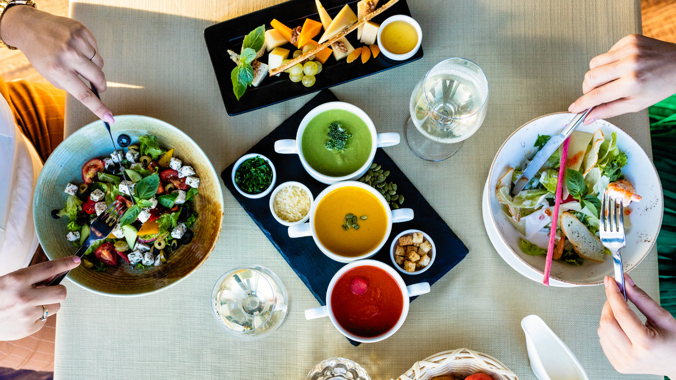 An overhead spread of people eating vibrant, healthy foods on a table with drinks