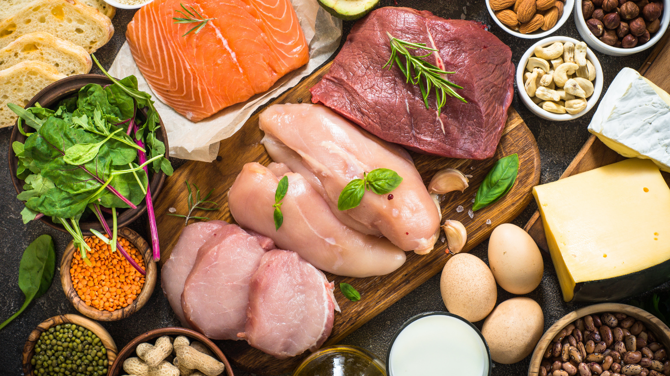 an array of high-protein foods spread out on a table including meats, beans, nuts, eggs, cheeses