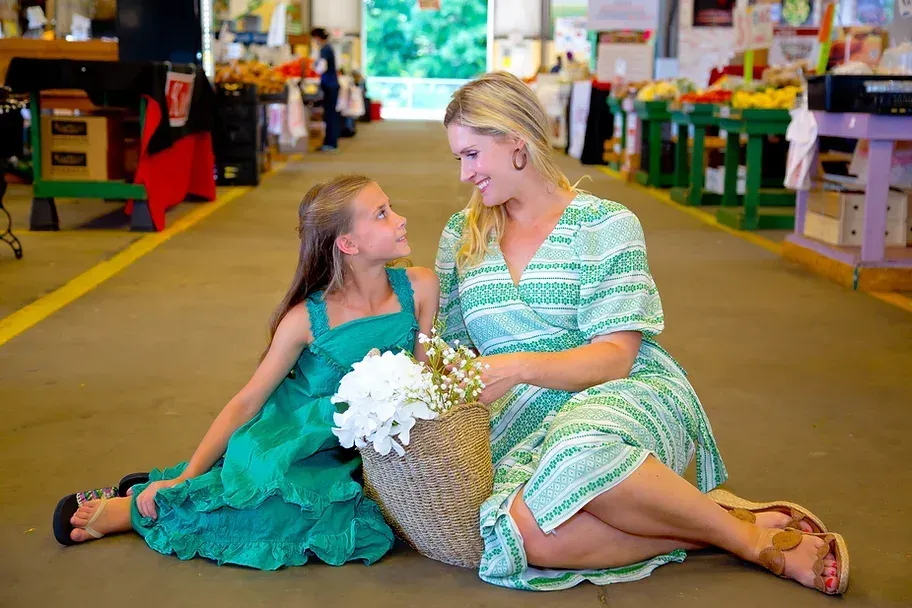 A woman and a little girl are sitting on the floor in a market.