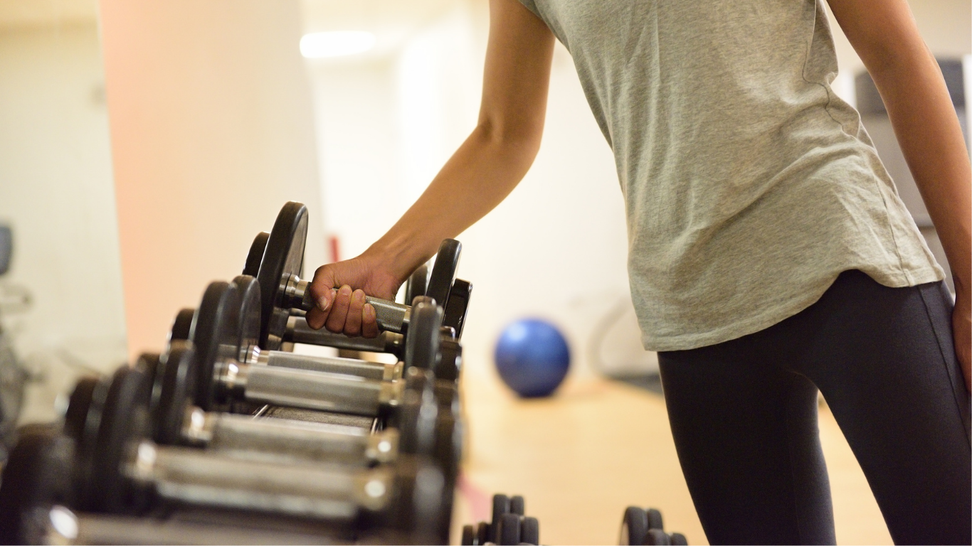 A woman reaches for a dumbbell on a weight rack in a gym