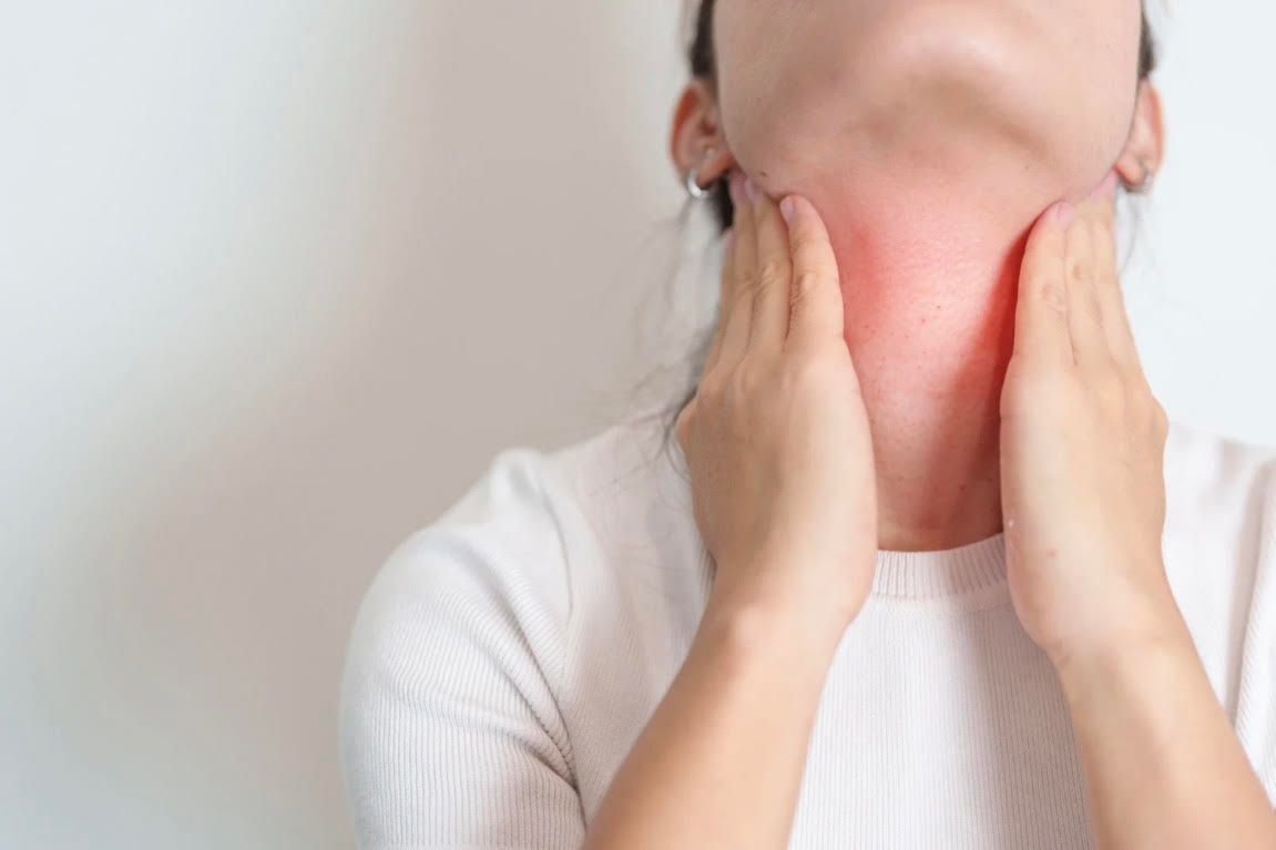 A woman is holding her neck in pain because of a sore throat.