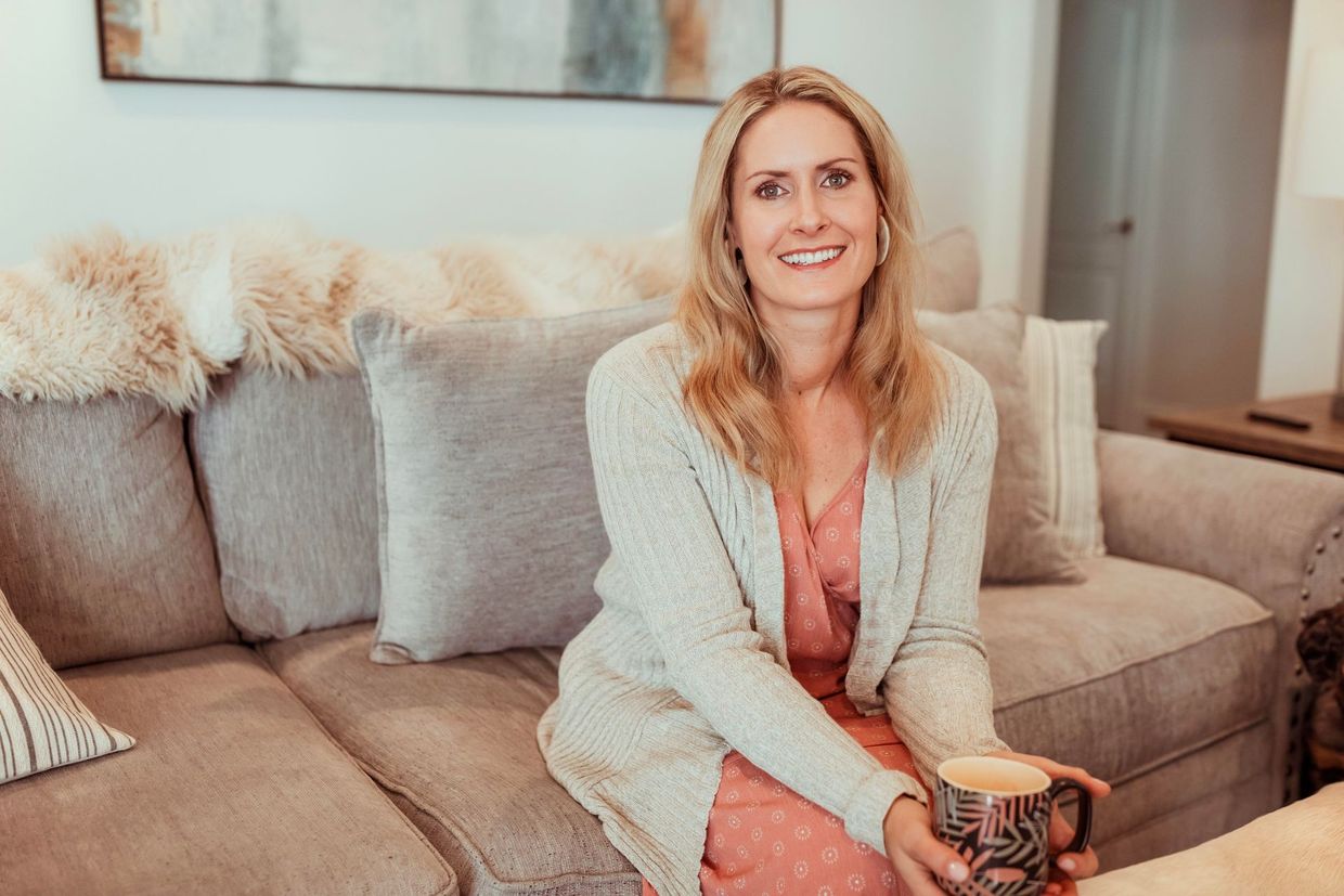 A woman is sitting on a couch holding a cup of coffee.