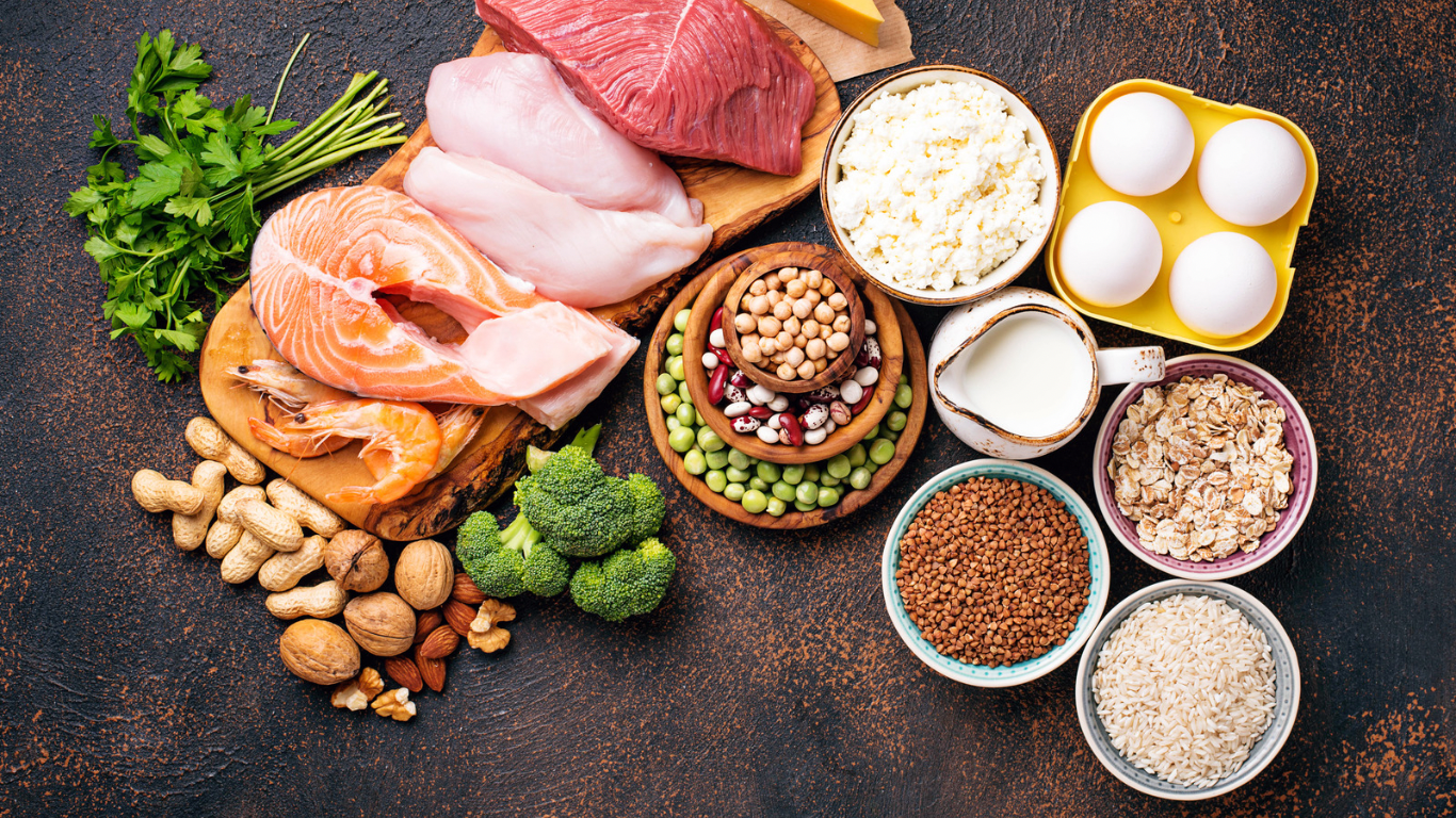 A spread of whole-foods based proteins including beans, and nuts are laid out with a dark background.