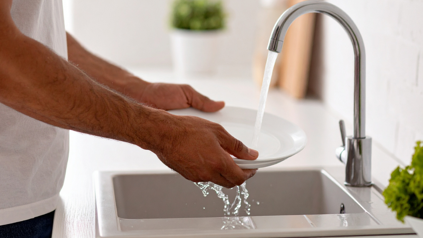 A man washes a white plate in a sink