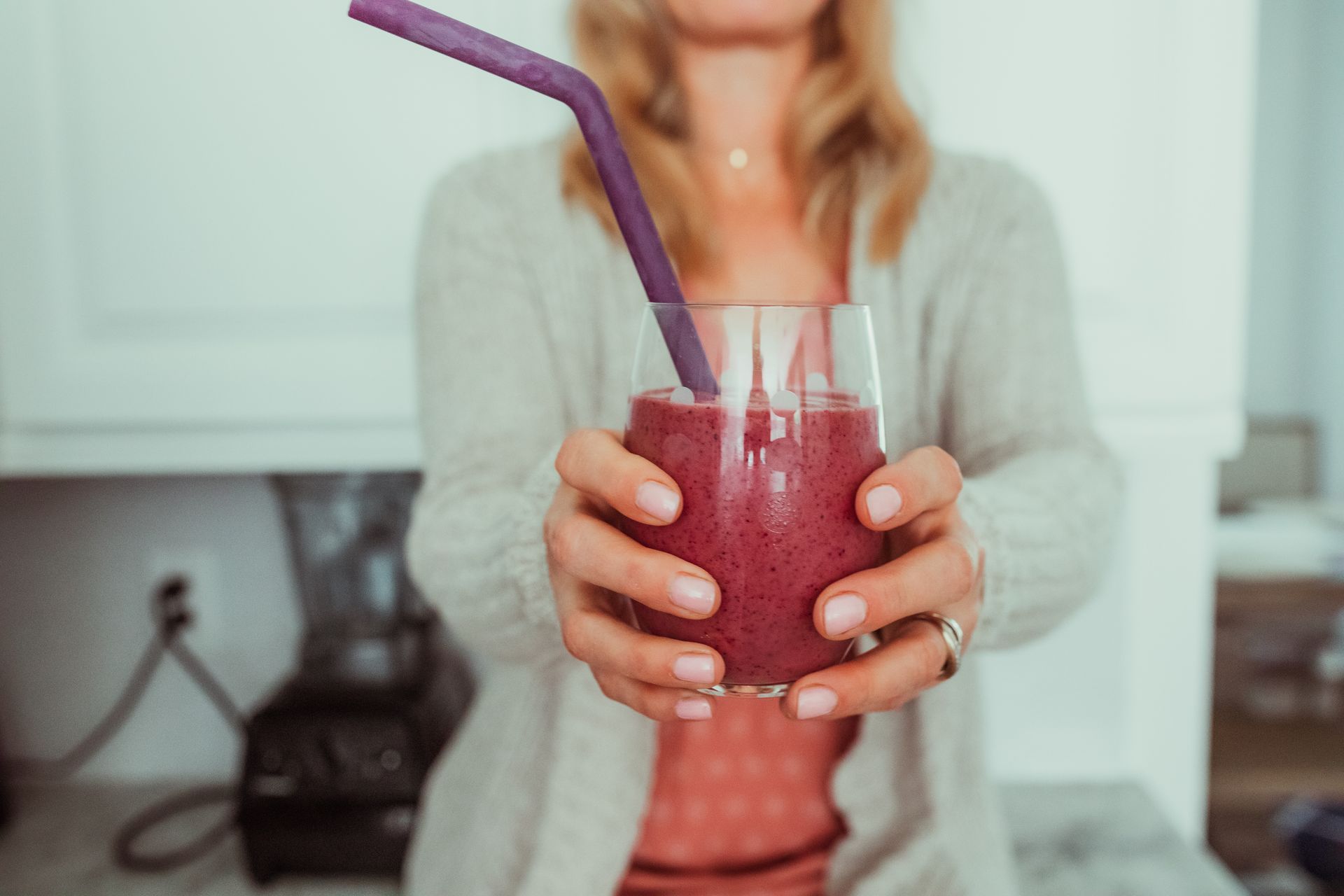 A woman is holding a glass of smoothie with a purple straw.