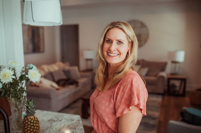 A woman in a pink dress is standing in a living room and smiling.