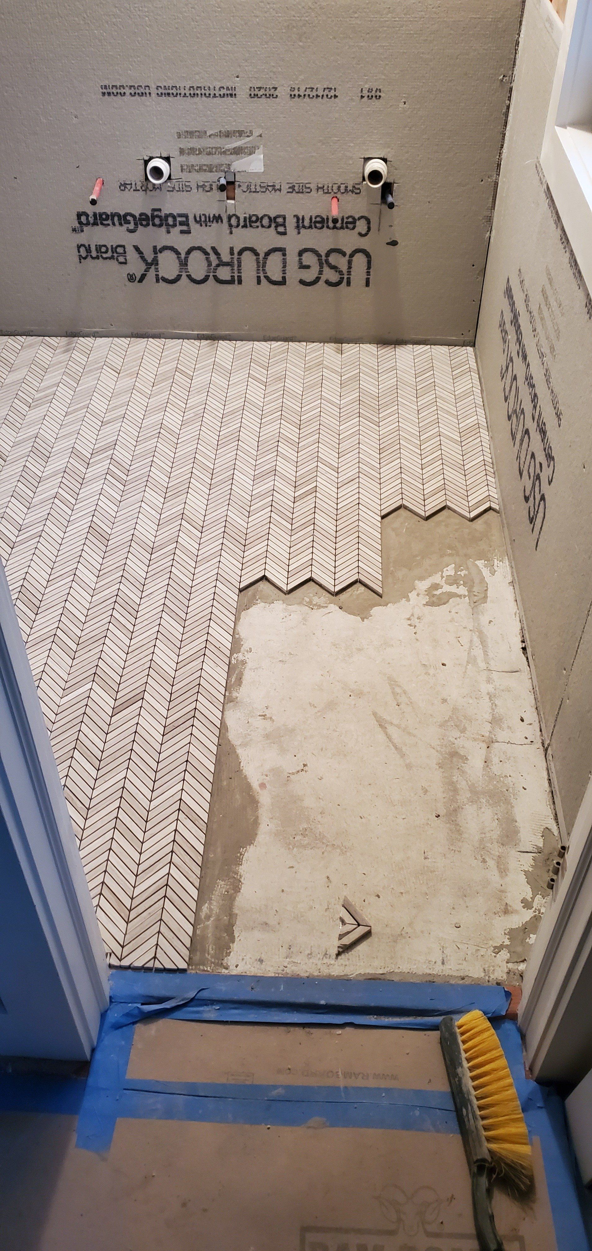 a bathroom floor is being tiled and a broom is sitting on the floor .