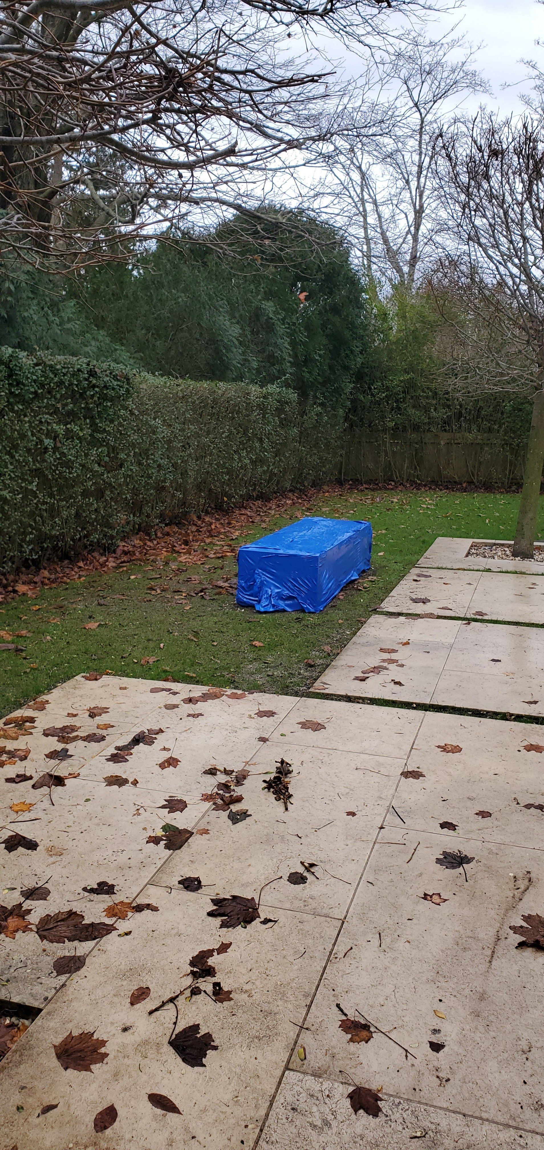 a box covered in blue shrink wrap sitting on the ground in a backyard .