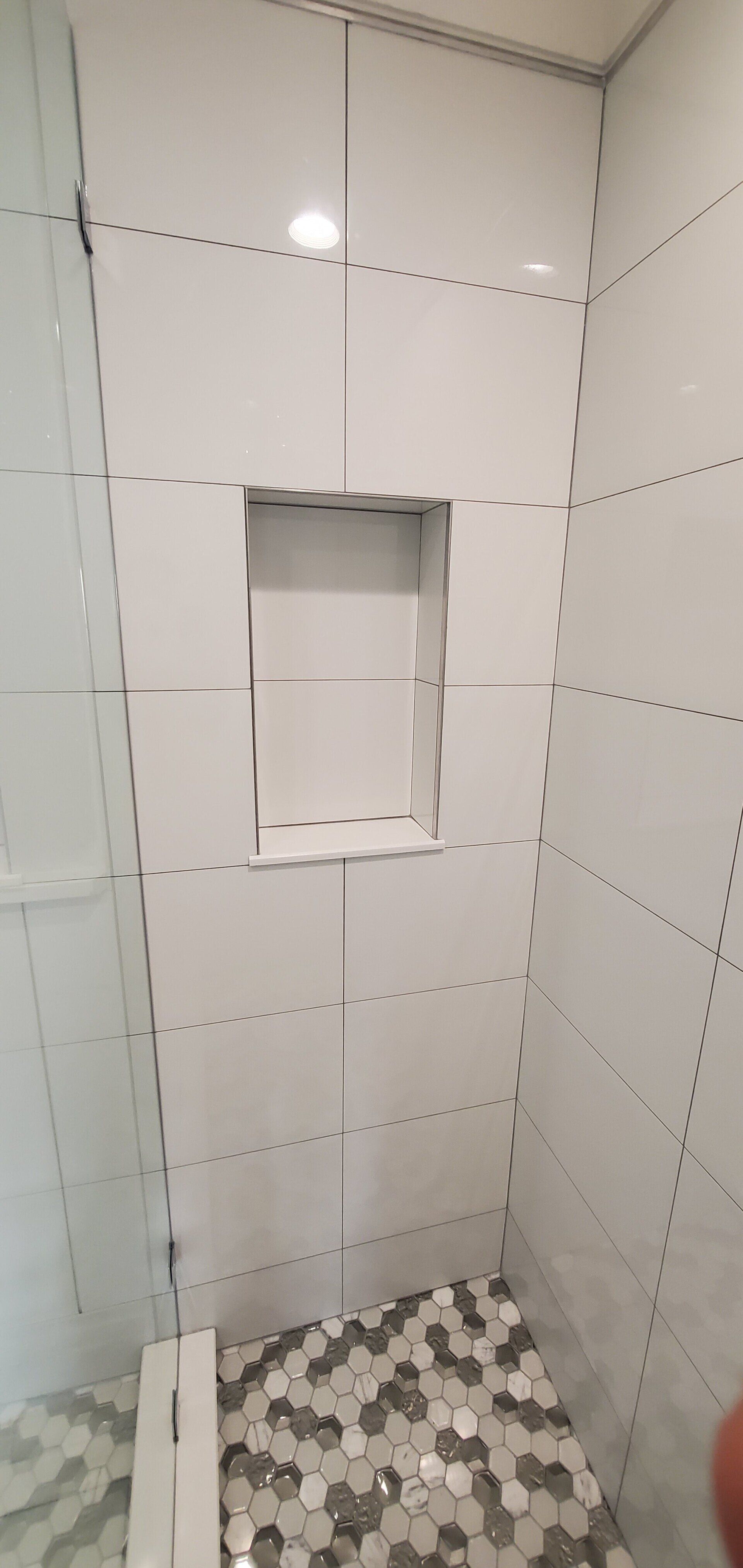 a shower stall with white tiles and a niche in the wall .