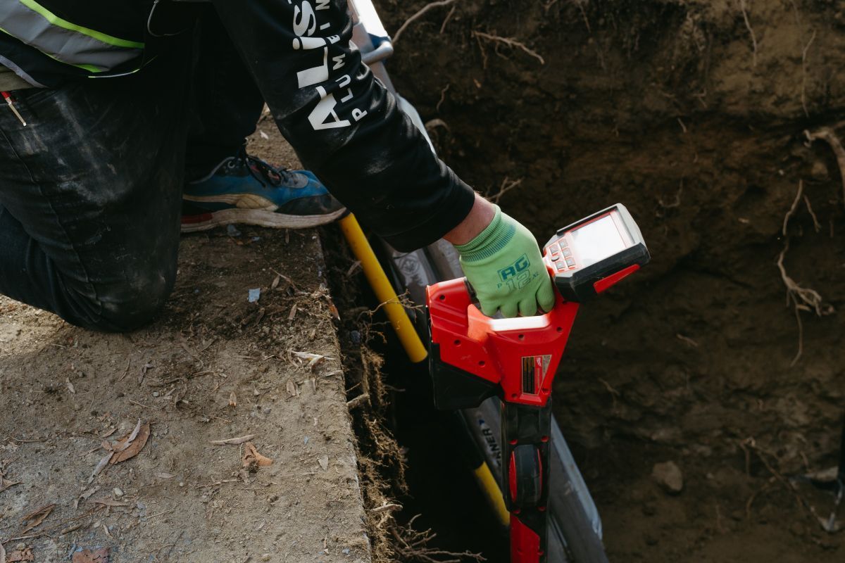A man is kneeling down in the dirt holding a tool.