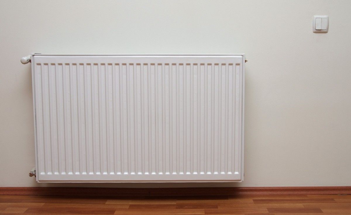 A white radiator is hanging on a white wall in an empty room.