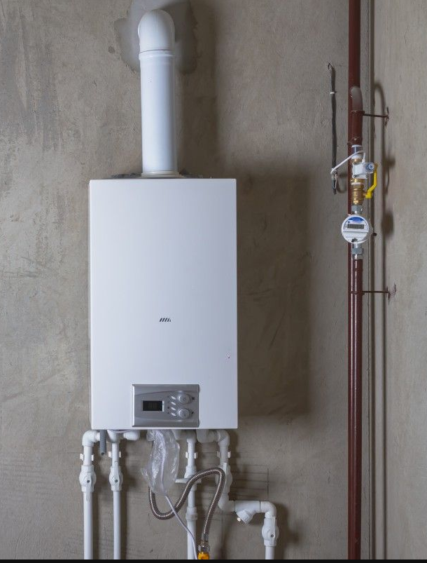 A white boiler is hanging on a wall next to pipes.
