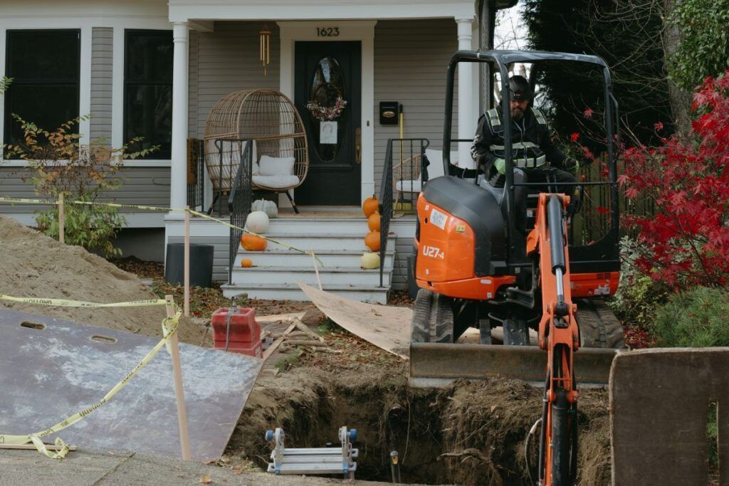 A man is driving an excavator in front of a house.