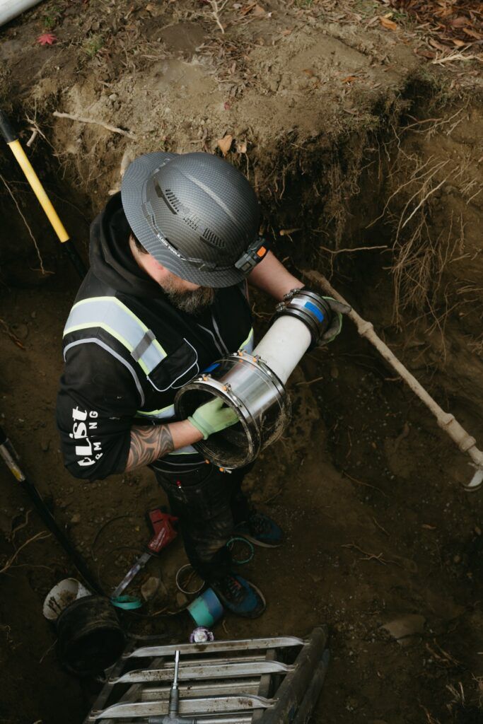 A man wearing a hard hat is working on a pipe in the dirt.