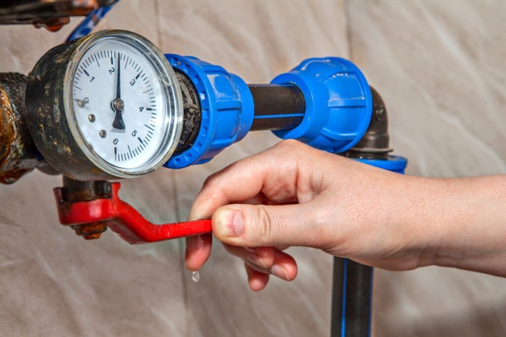 A person is adjusting a pressure gauge on a water pipe.