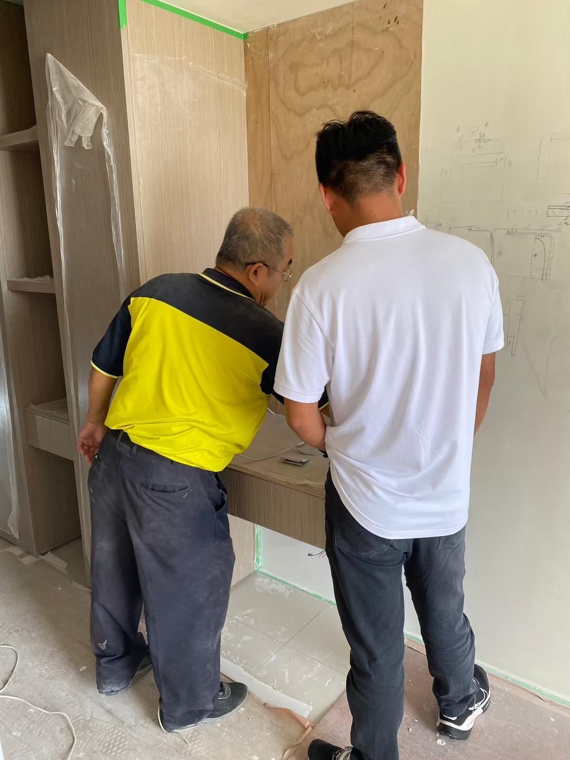 Two men are working on a wall in a room.
