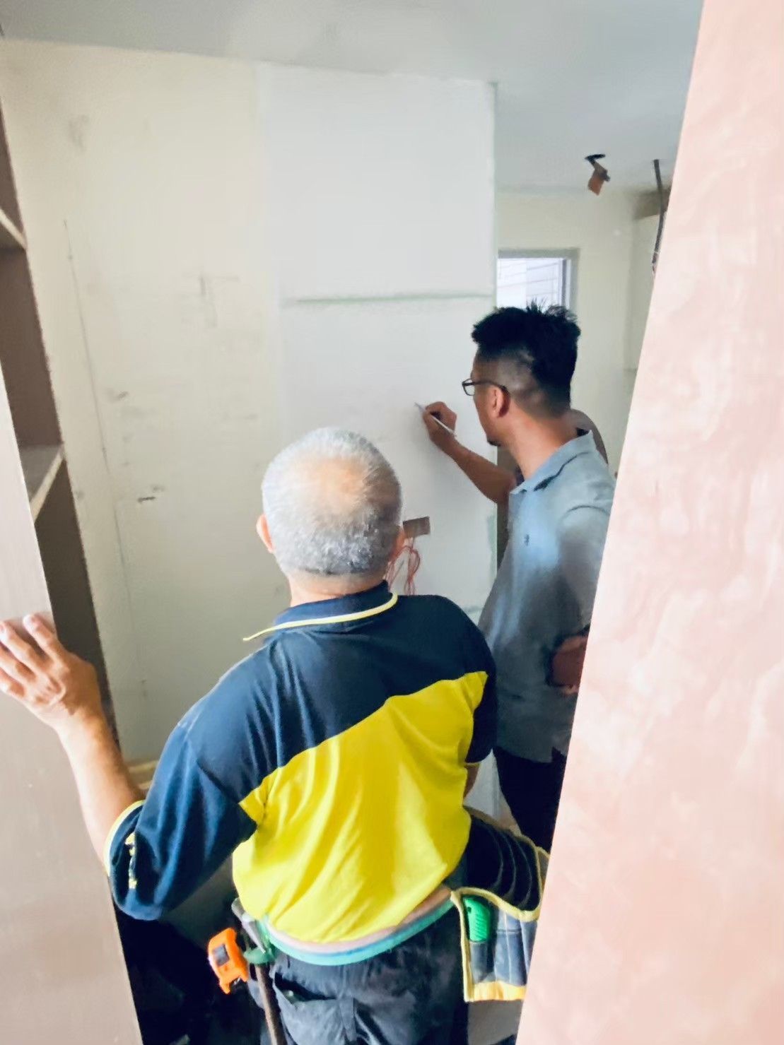 Two men are working on a wall in a room.