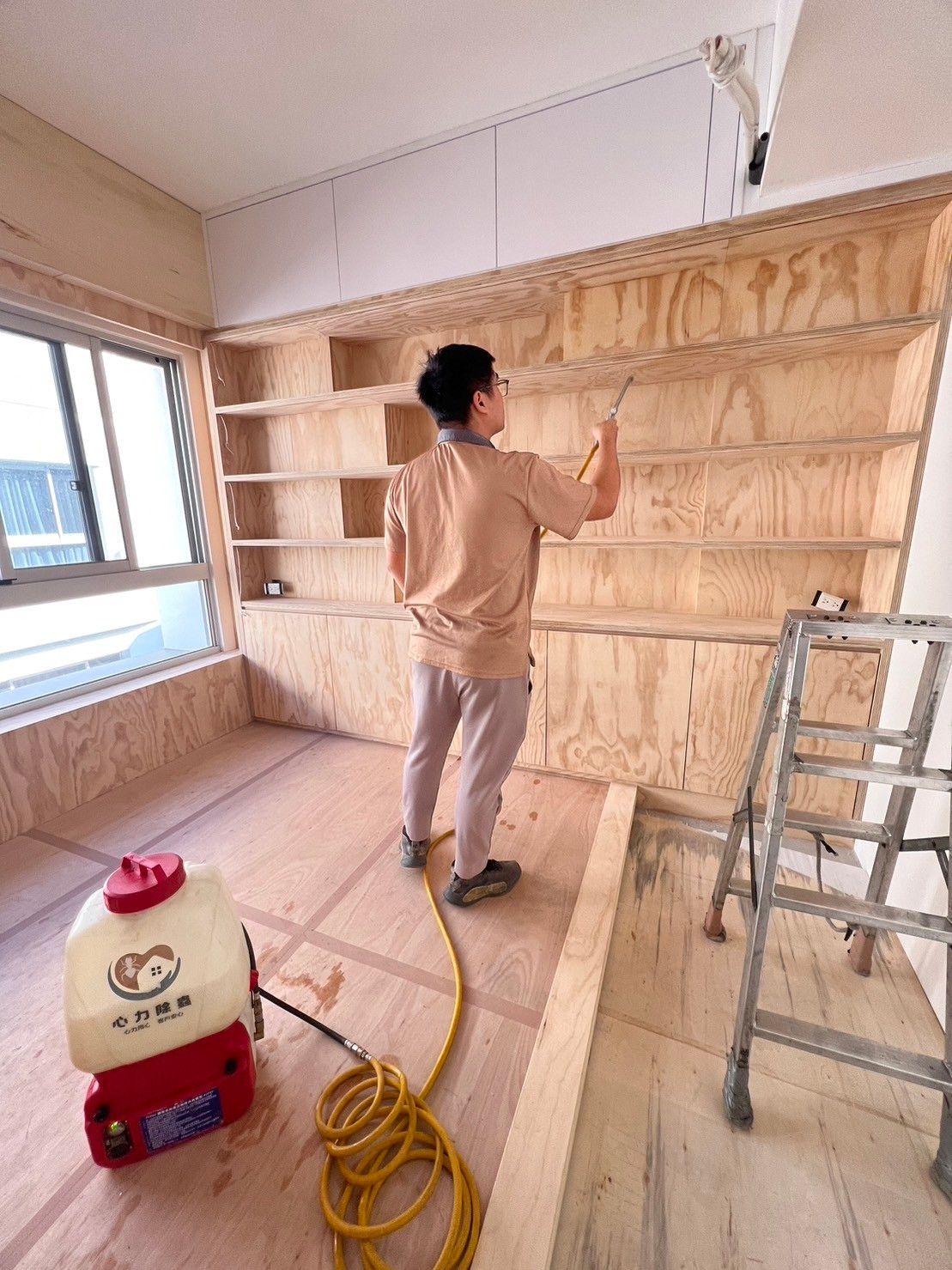 A man is spraying a wall with a sprayer in a room.
