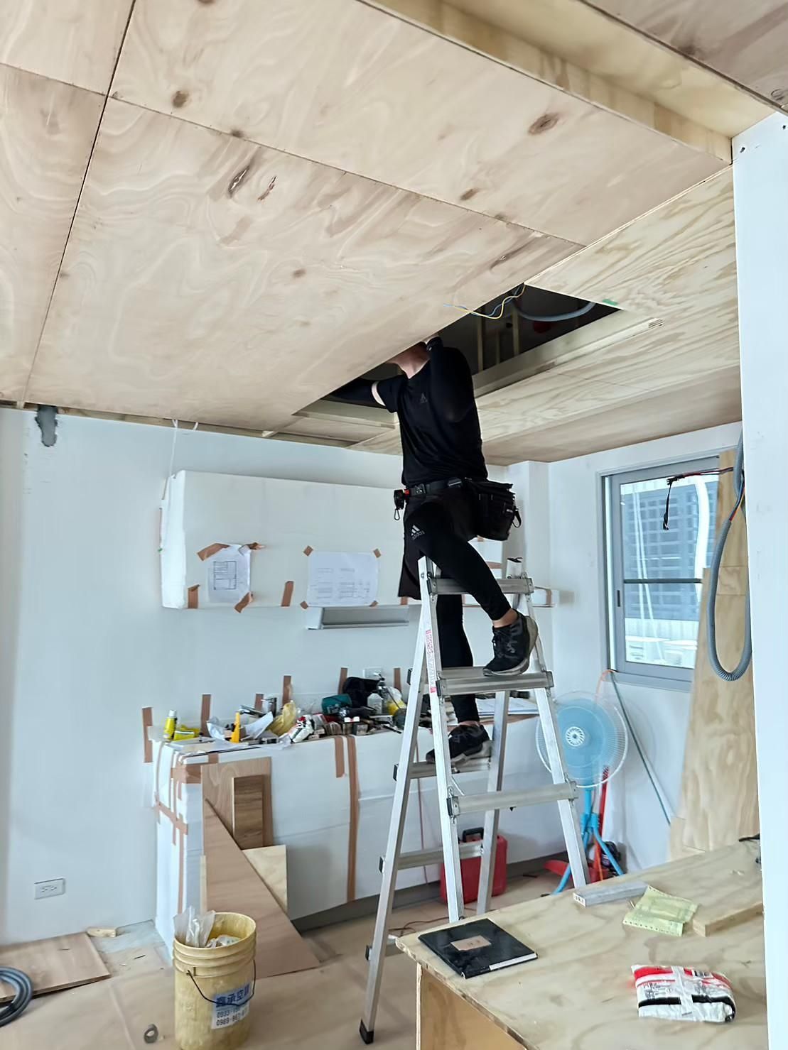 A man is standing on a ladder working on a wooden ceiling.