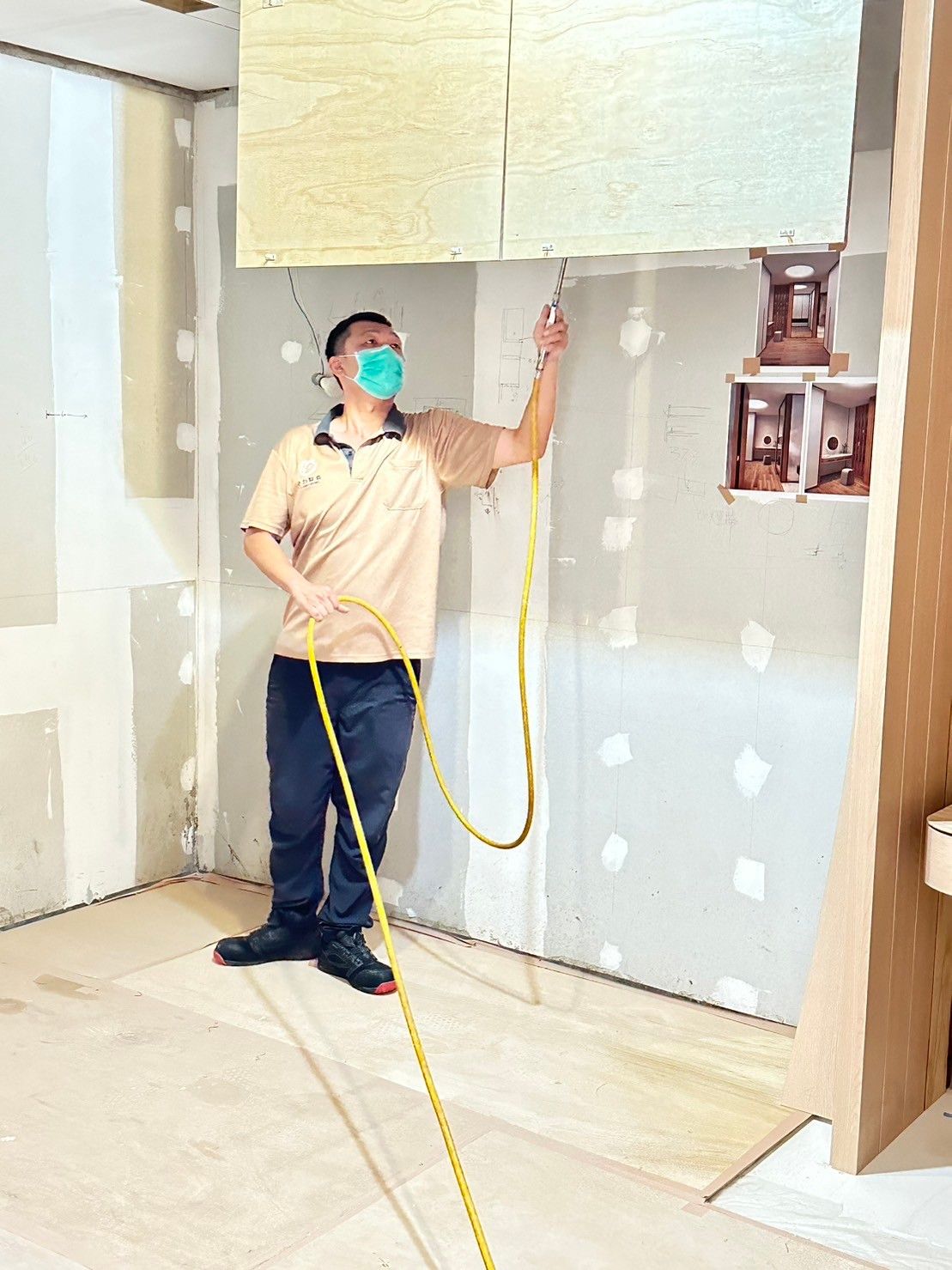 A man wearing a mask is measuring a wall with a tape measure.