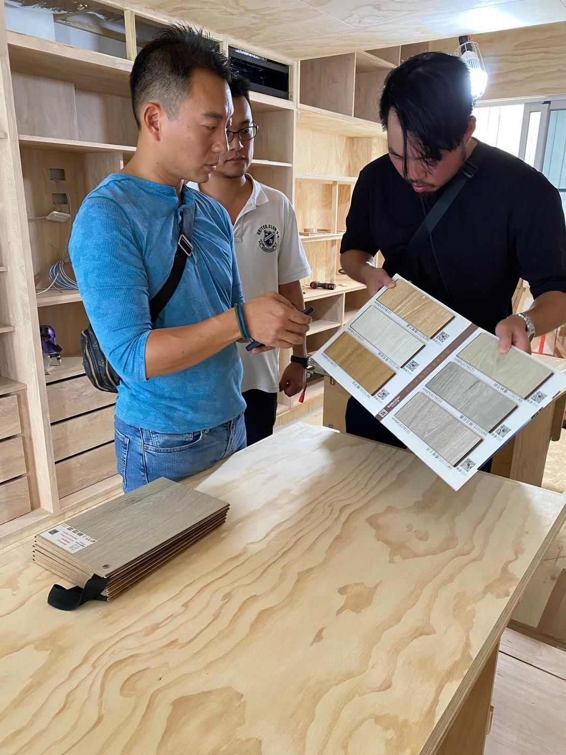 Three men are looking at a catalog of wood samples.