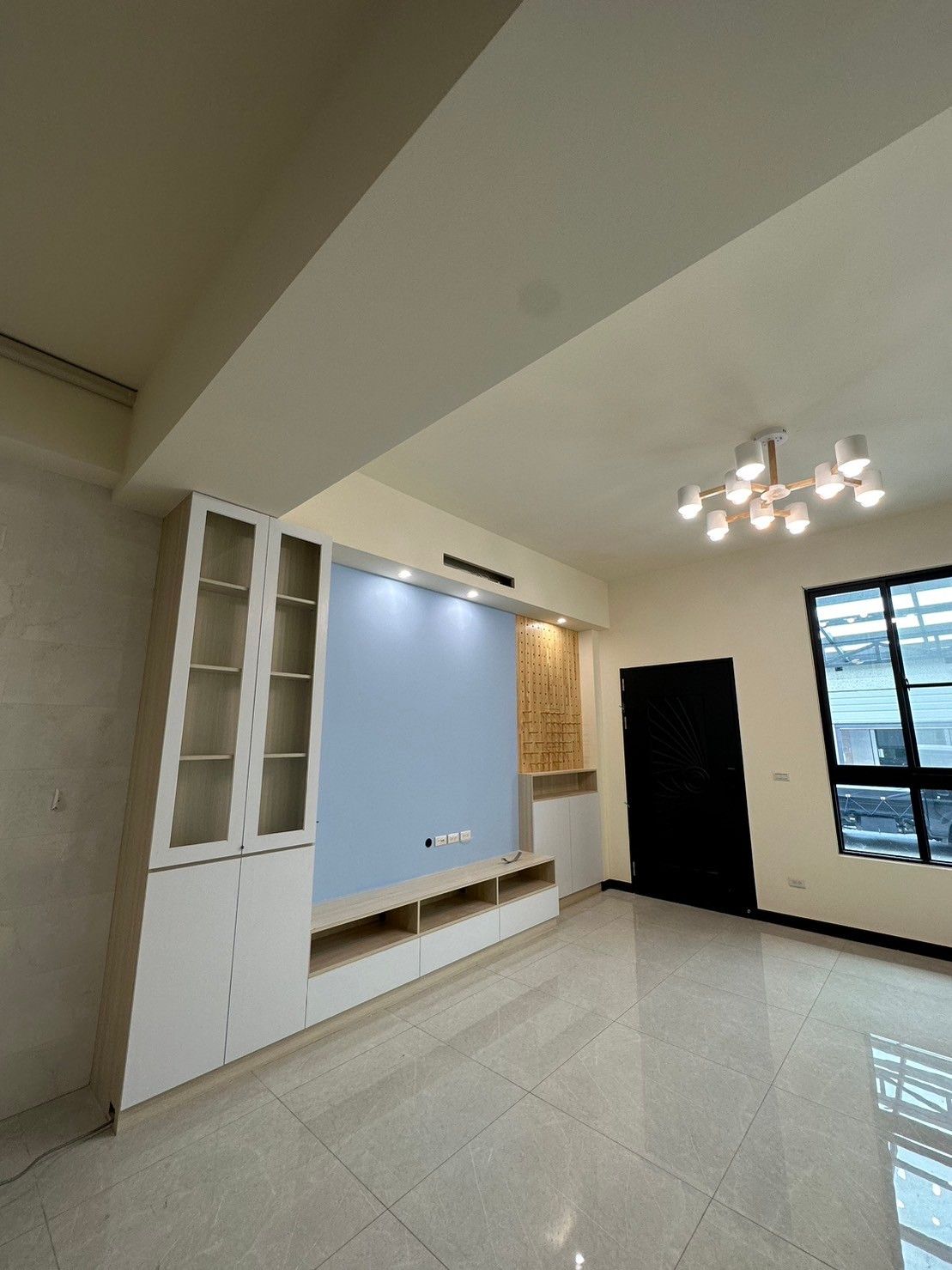 A living room with a television on the wall and a chandelier hanging from the ceiling.