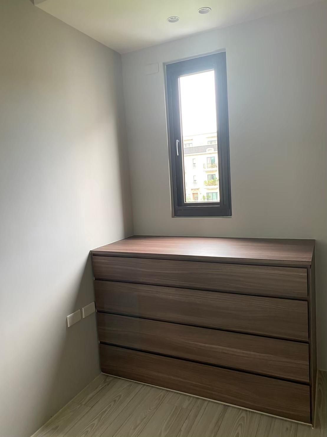 There is a dresser in the middle of the room with a window.