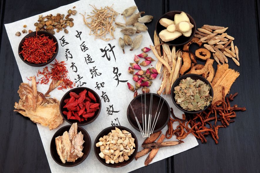Overhead shot of various dried herbs and spices, acupuncture needles, and calligraphy on paper.