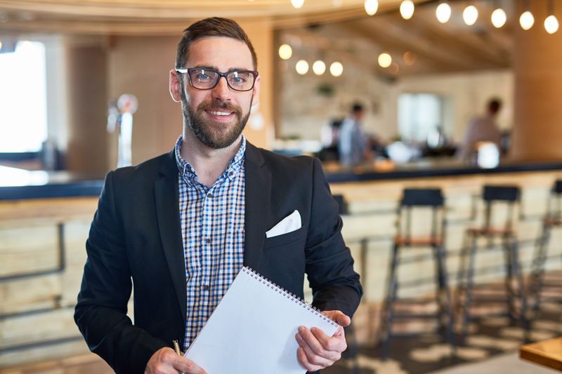 Man in a dark blazer holding papers in a bright modern office lounge with blurred seating behind him