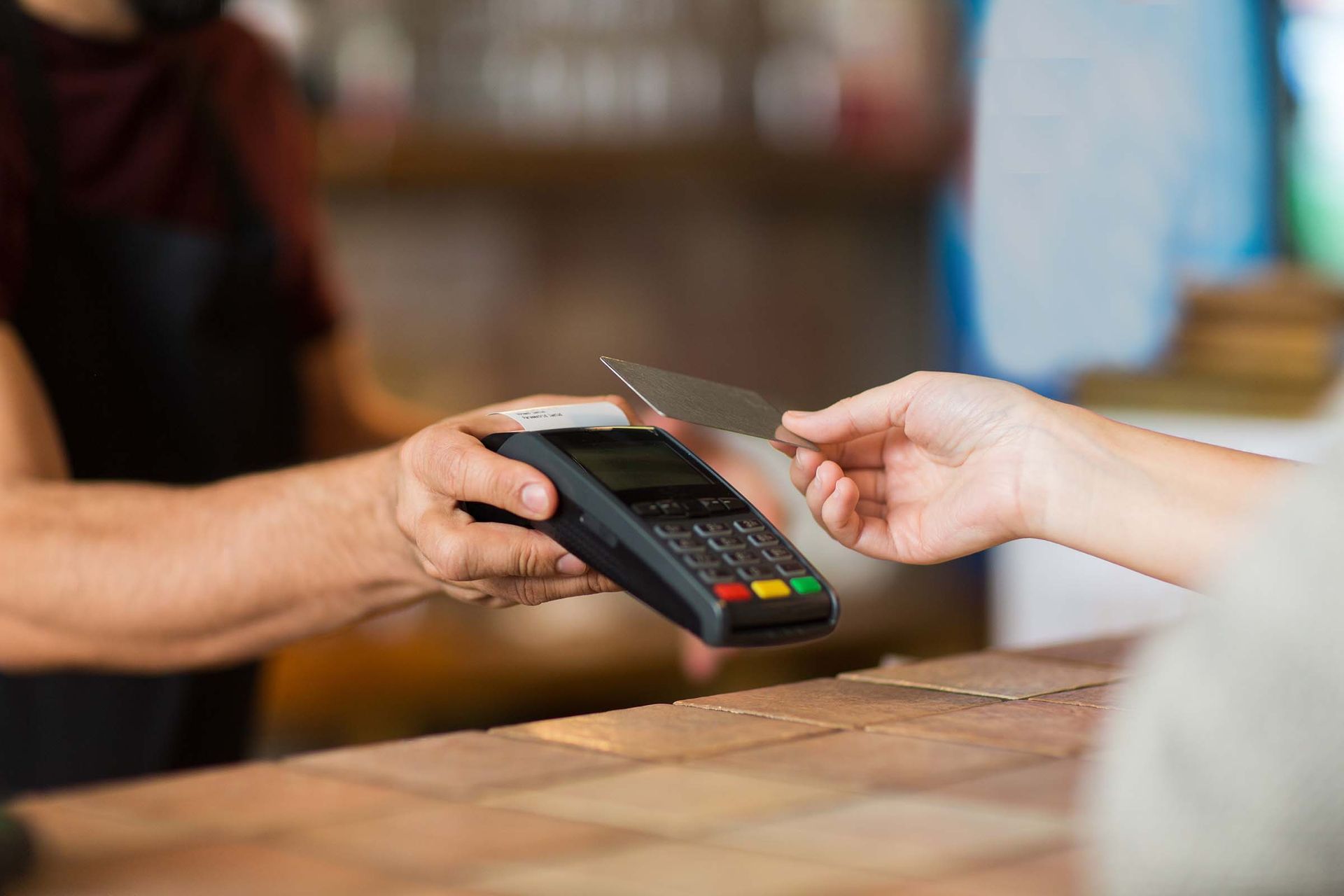 Customer tapping card on payment terminal as cashier holds the device at a counter