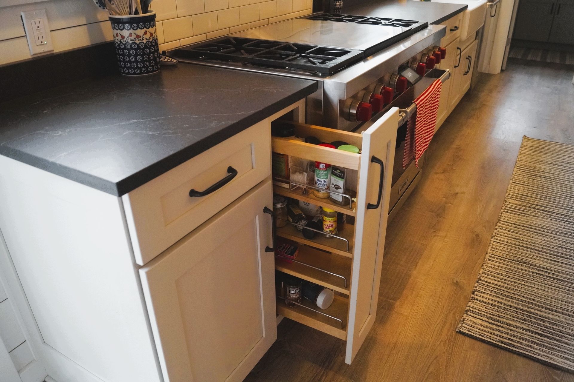 White kitchen cabinets with black handles under a countertop, above a wooden floor.