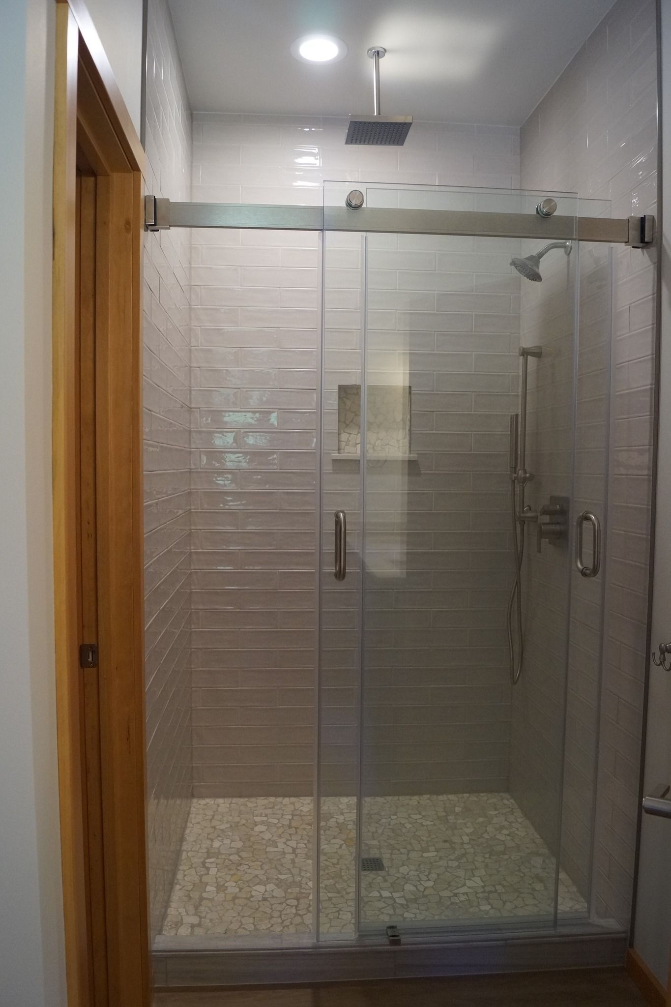 Modern glass shower enclosure with tiled walls and pebble floor in a bathroom