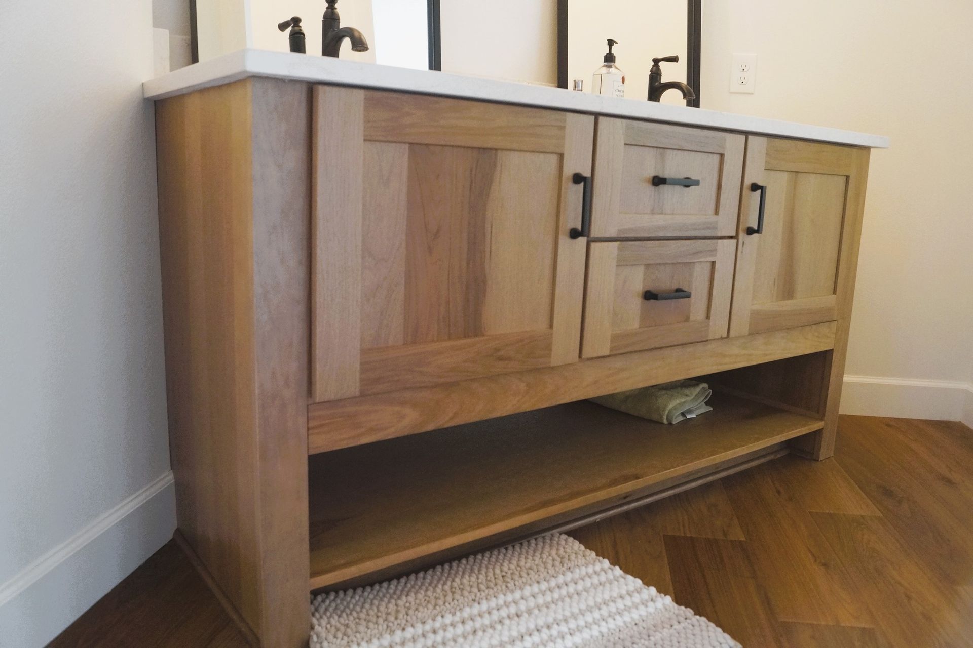 Wooden bathroom vanity with double sinks, drawers, and an open shelf on a hardwood floor.