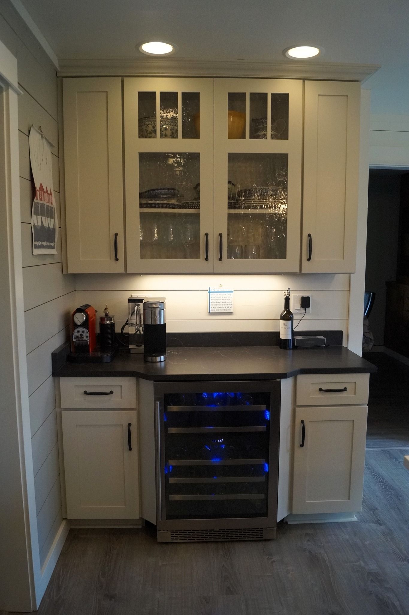 Small kitchen with white cabinets, black countertops, built-in wine fridge, and under-cabinet lighting.