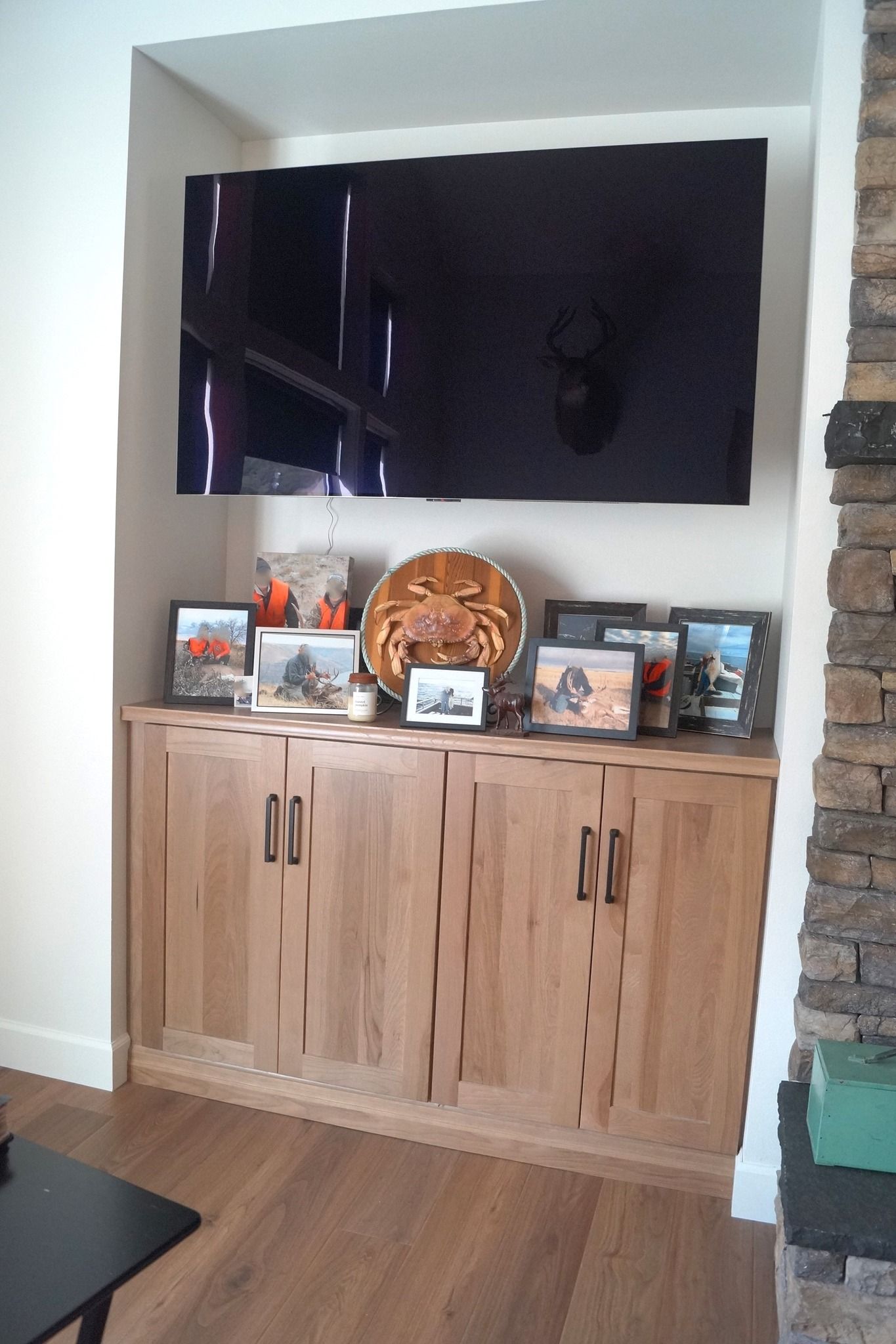 Built-in wooden cabinet with framed photos and a wicker basket in a recessed wall alcove