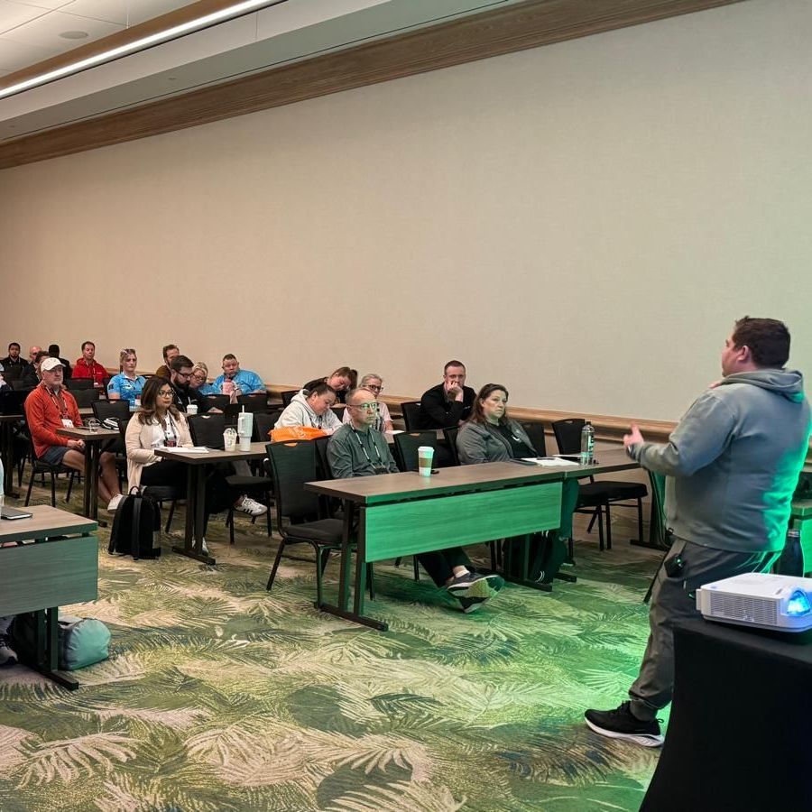 A man is giving a presentation to a group of people sitting at tables in a conference room.