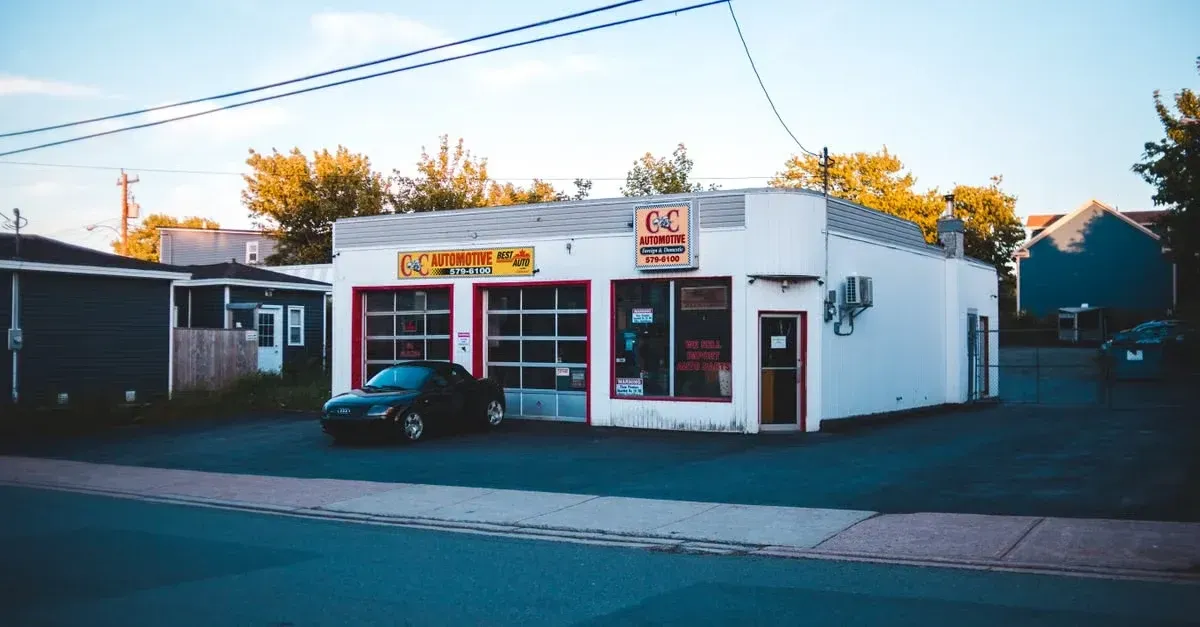 Classic automotive repair shop with red garage doors and signage during golden hour sunset.