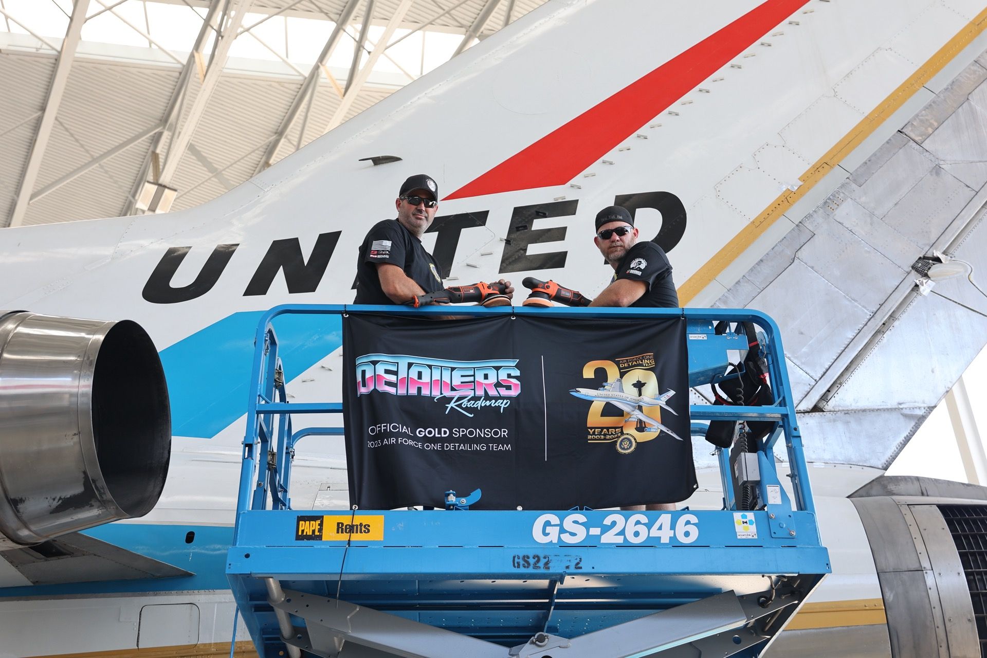 Two men are sitting on a lift in front of a united airplane.