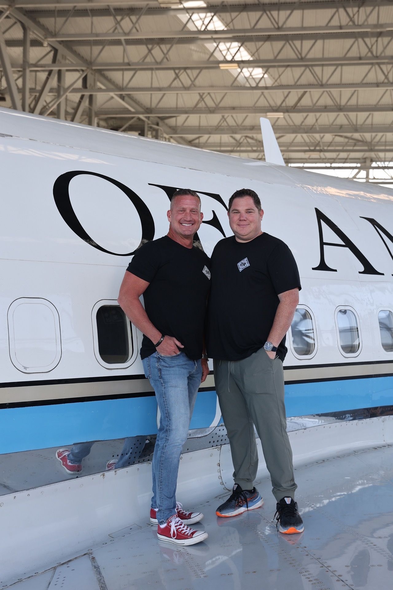 Two men are standing in front of an airplane in a hangar.