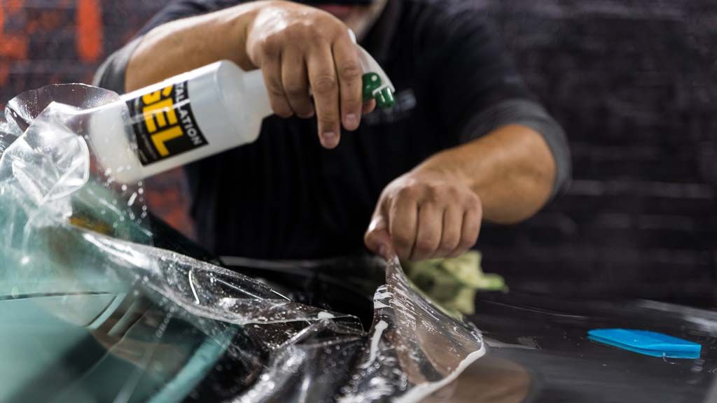 a man is spraying a bottle of gel on a car windshield .