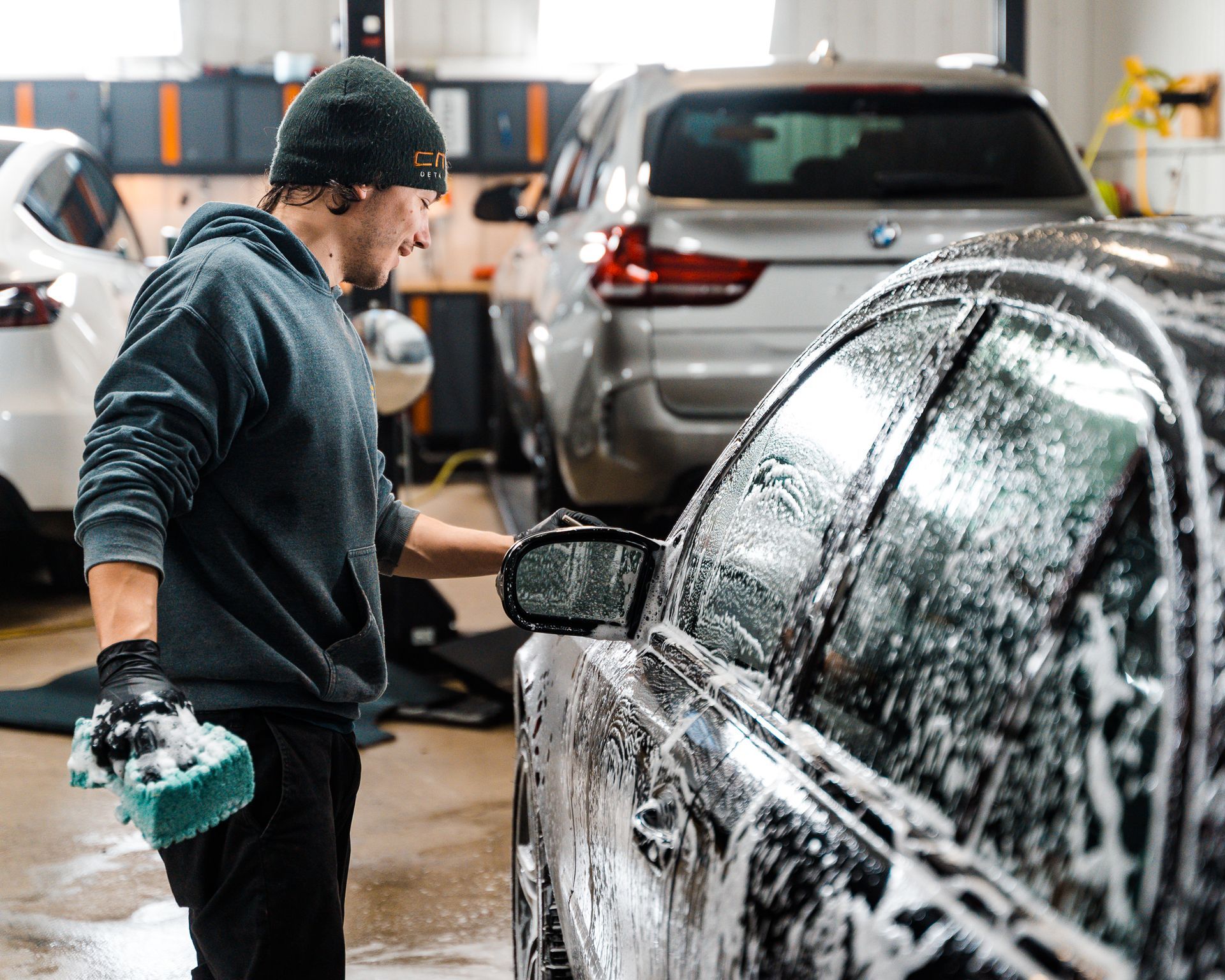 A man is washing a car with a sponge in a garage.